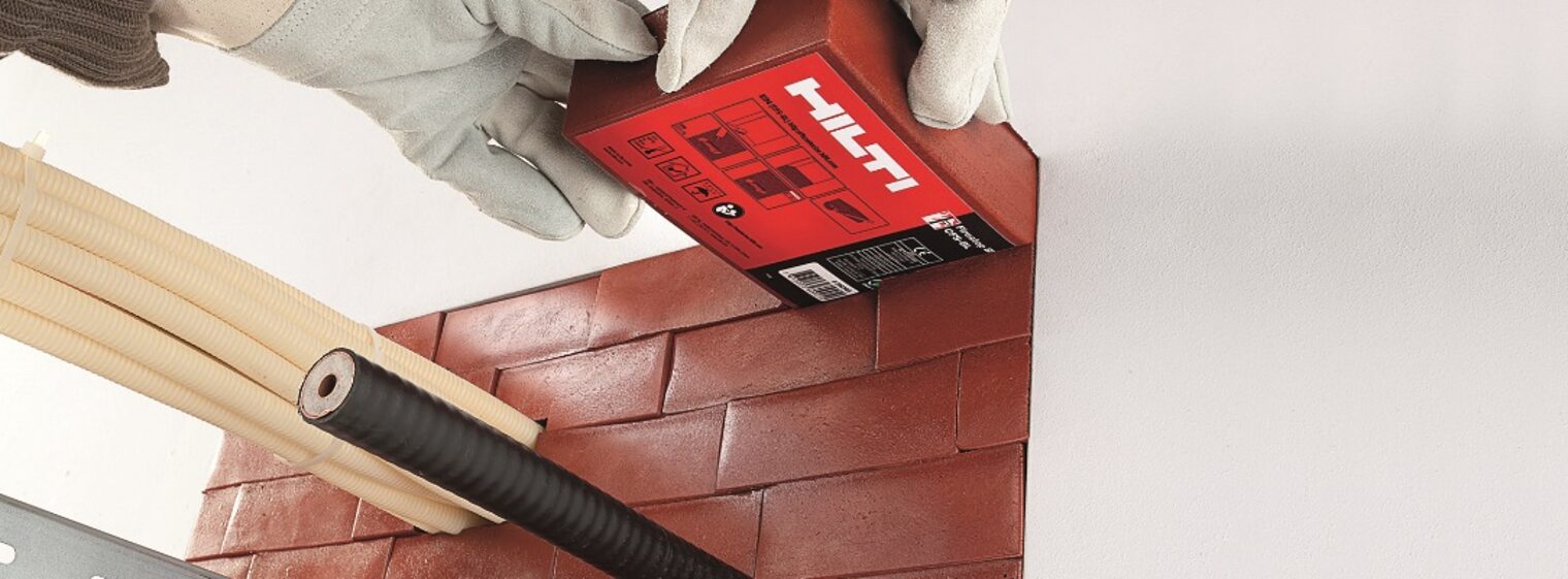 Ein Brandschutzstein von HILTI wird in einen Brandschott eingefügt. Aus den Brandschutzsteinen ragen Leitungen und Trockenbauelemente heraus