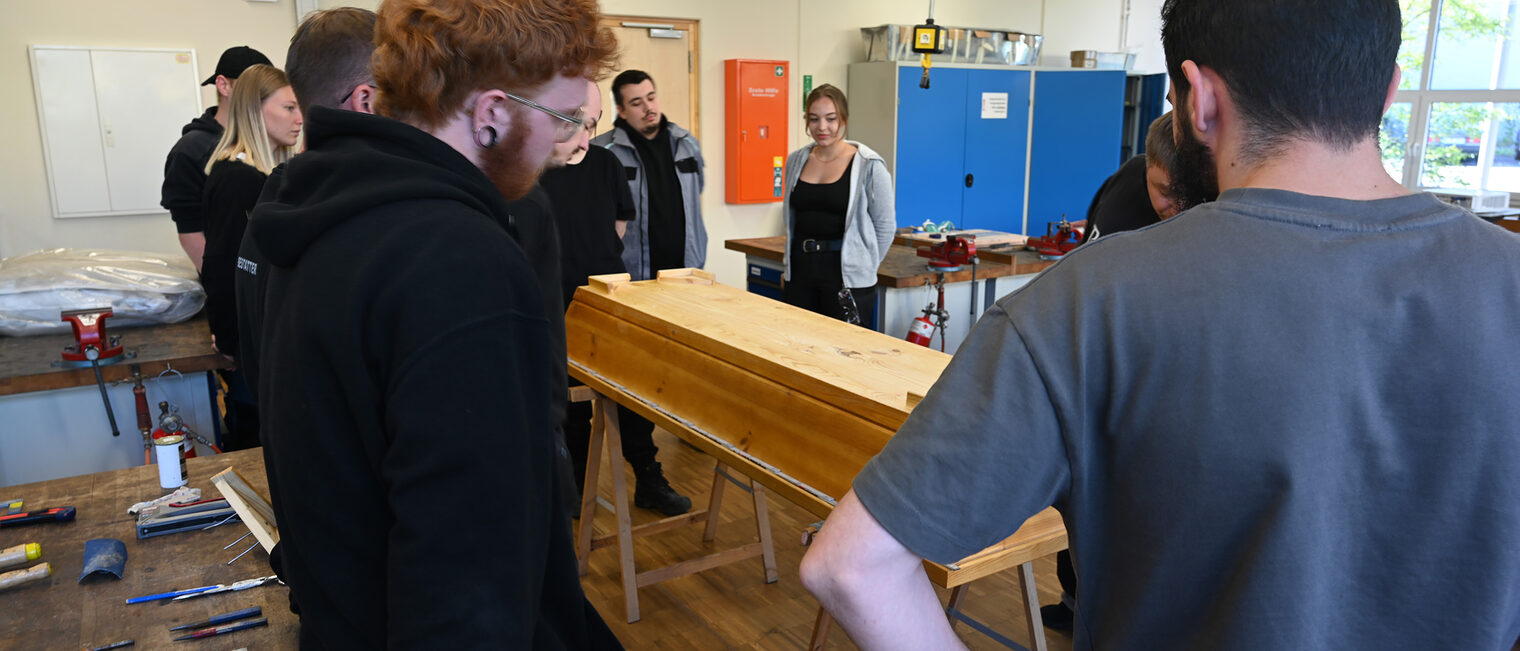 Auszubildende im Bestatterhandwerk stehen um einen Sarg