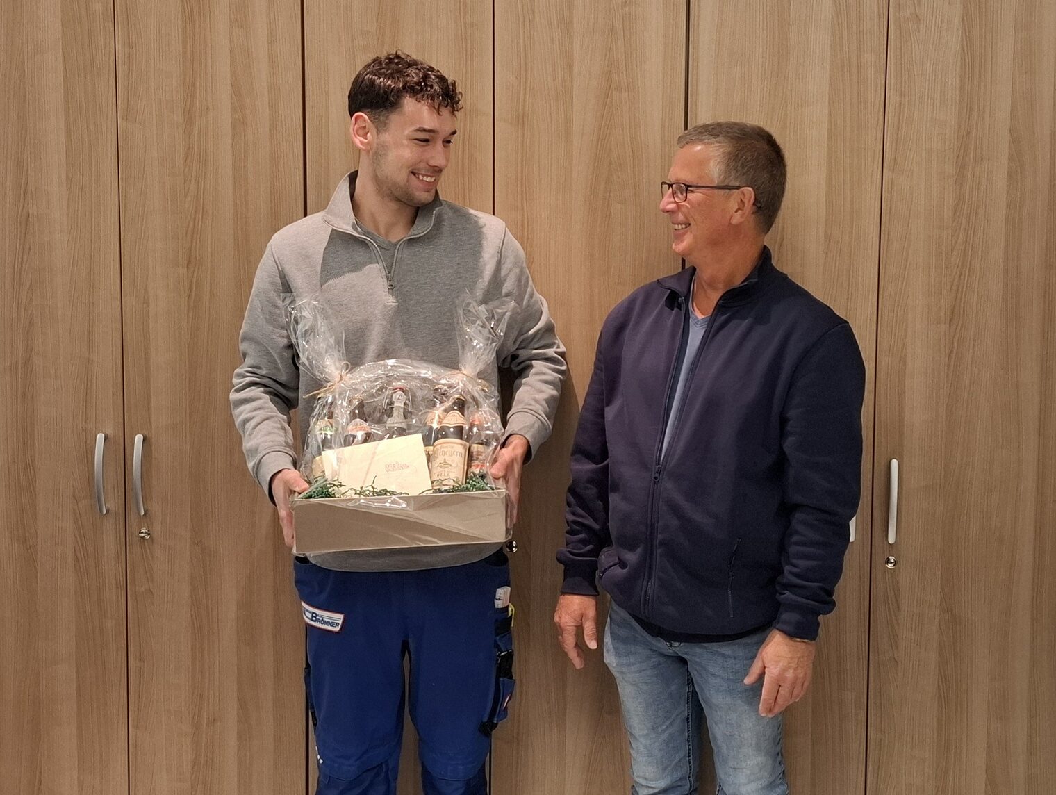Sieger und Betriebsinhaber mit Geschenkkorb vor Wand