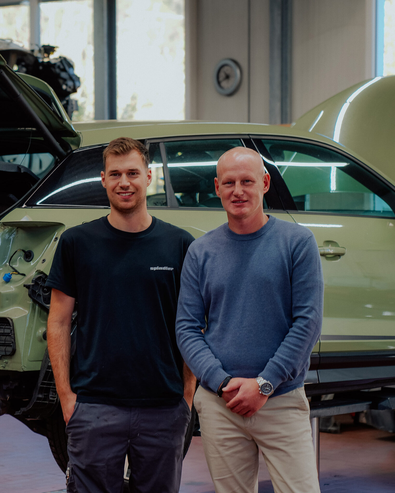 Geselle und Ausbilder vor Karosserie schauen in Kamera