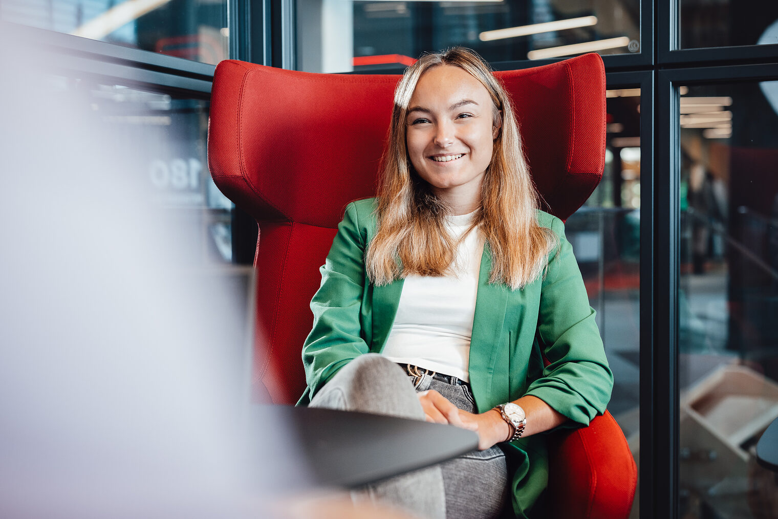 Frau in grünem Jackett mit mittellangen hellbraunen Haaren sitzt auf rotem Sessel, lächelt