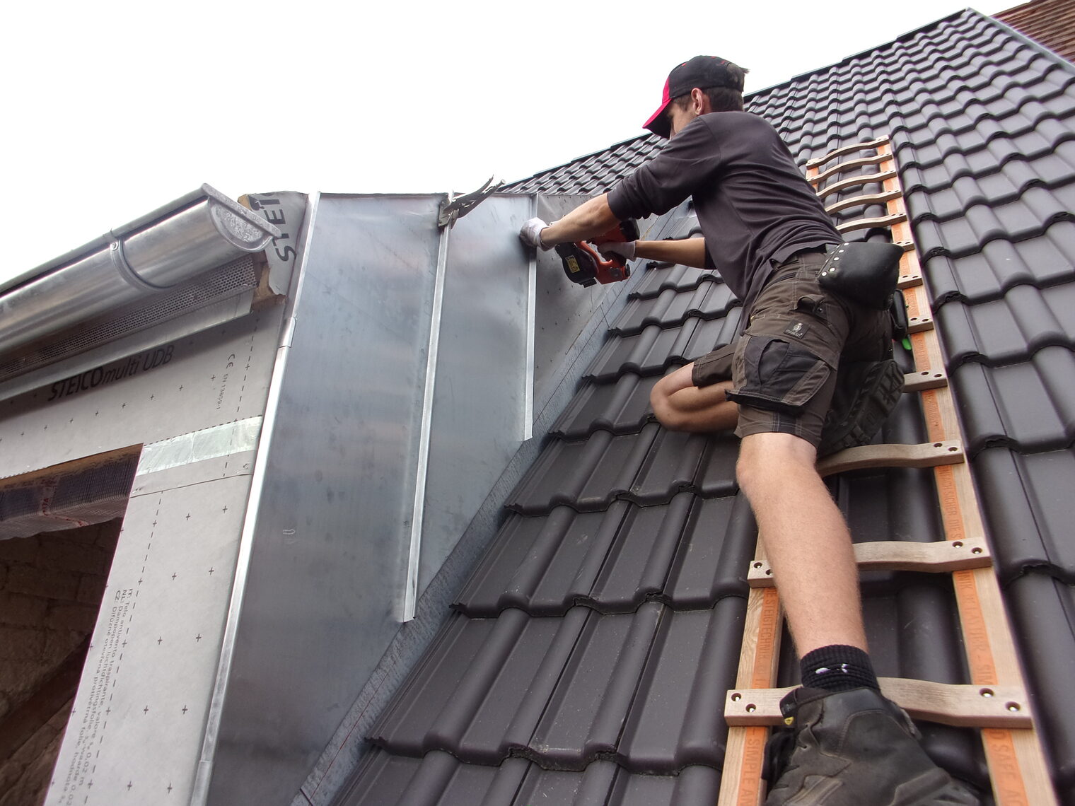 Junger Mann auf Leiter auf Dach arbeitet an Hausfassade