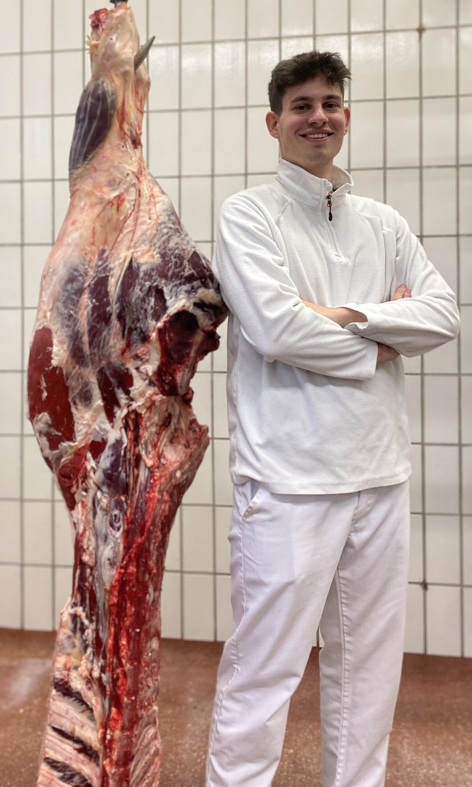 Junger Mann steht mit verschränkten Armen lächelnd neben einem zerlegten Tier