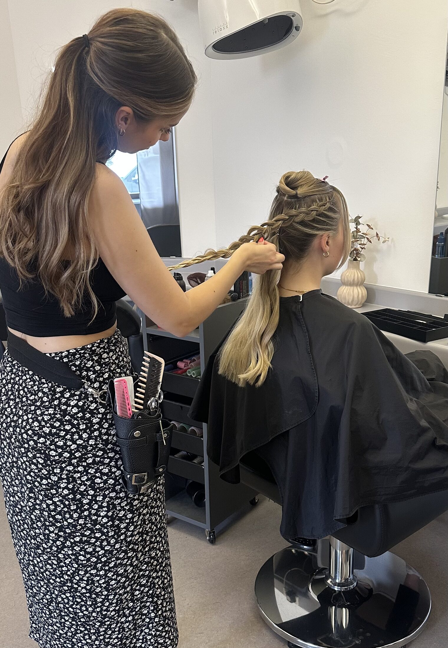Friseurin flechtet einer Kundin die langen Haare, Foto aufgenommen von hinten