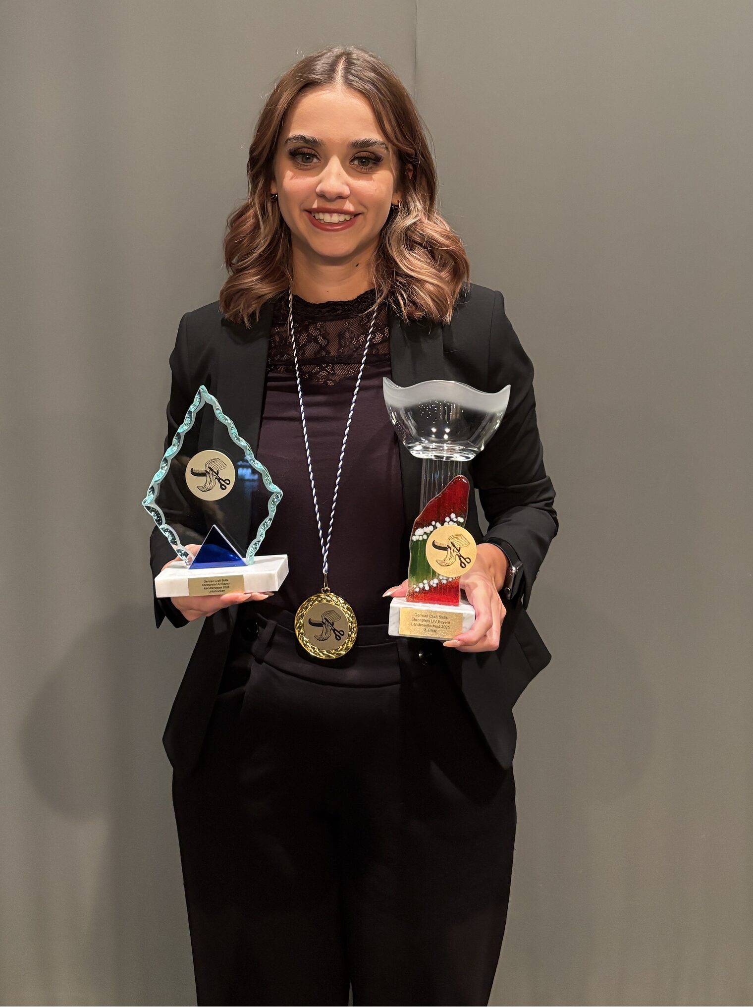 Junge Frau stehend mit zwei Pokalen in den Händen und einer Medallie um den Hals