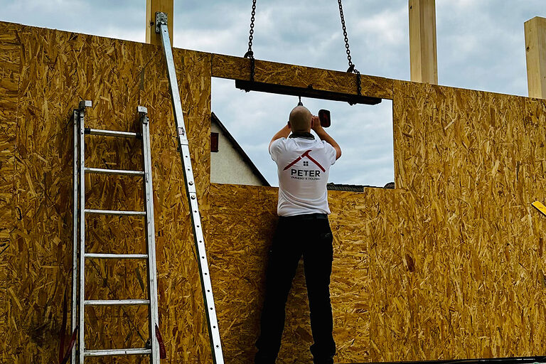 Zimmerer auf Baustelle an Holzwand, schreibt auf Plan