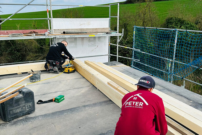 Baustelle, oben auf dem Dach, zwei Zimmerer arbeiten an Holzbalken
