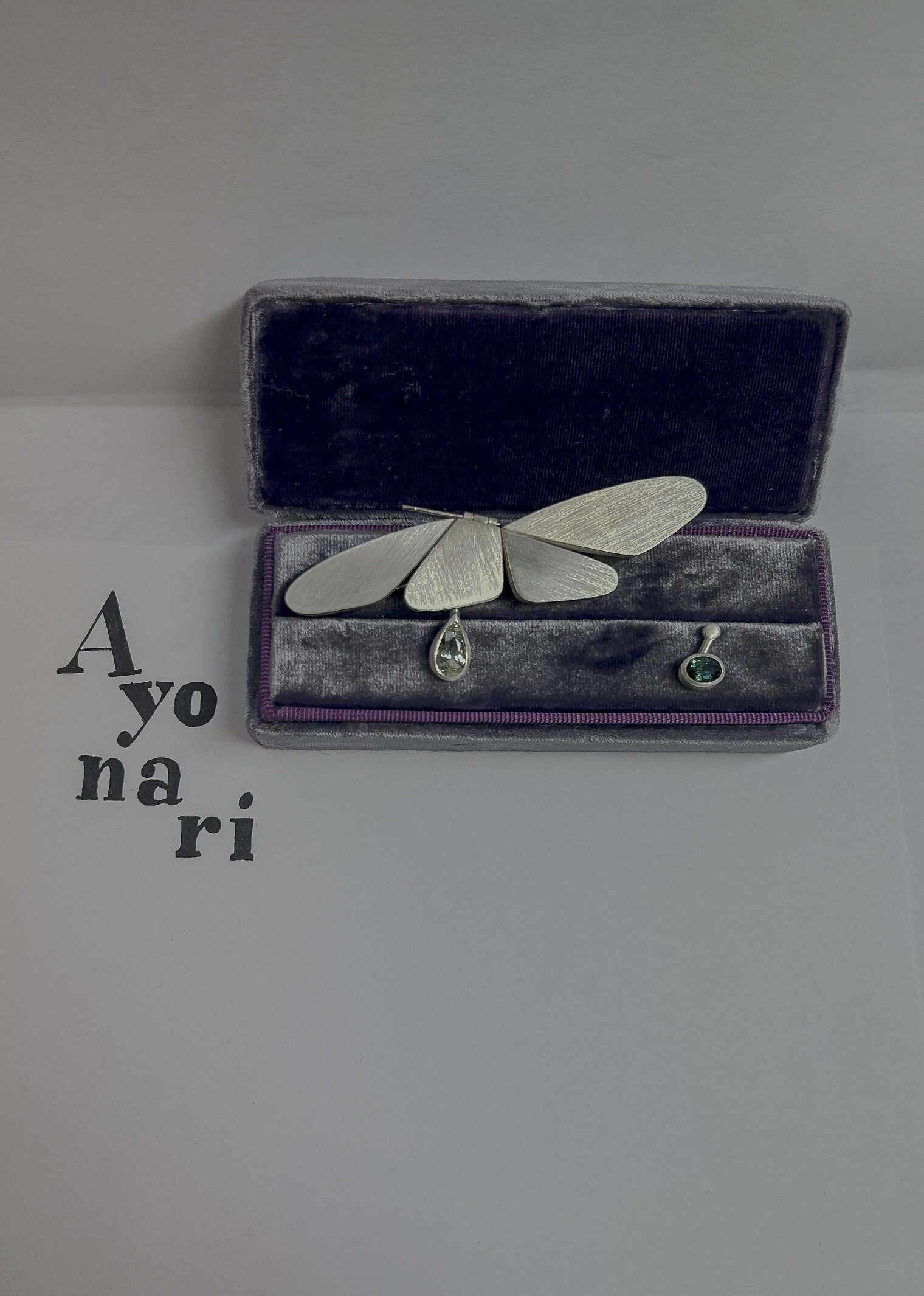 Schmuckstück in Schatulle mit Ähnlichkeit zu Schmetterling, grüner Stein eingefasst, Text "A yo na ri"