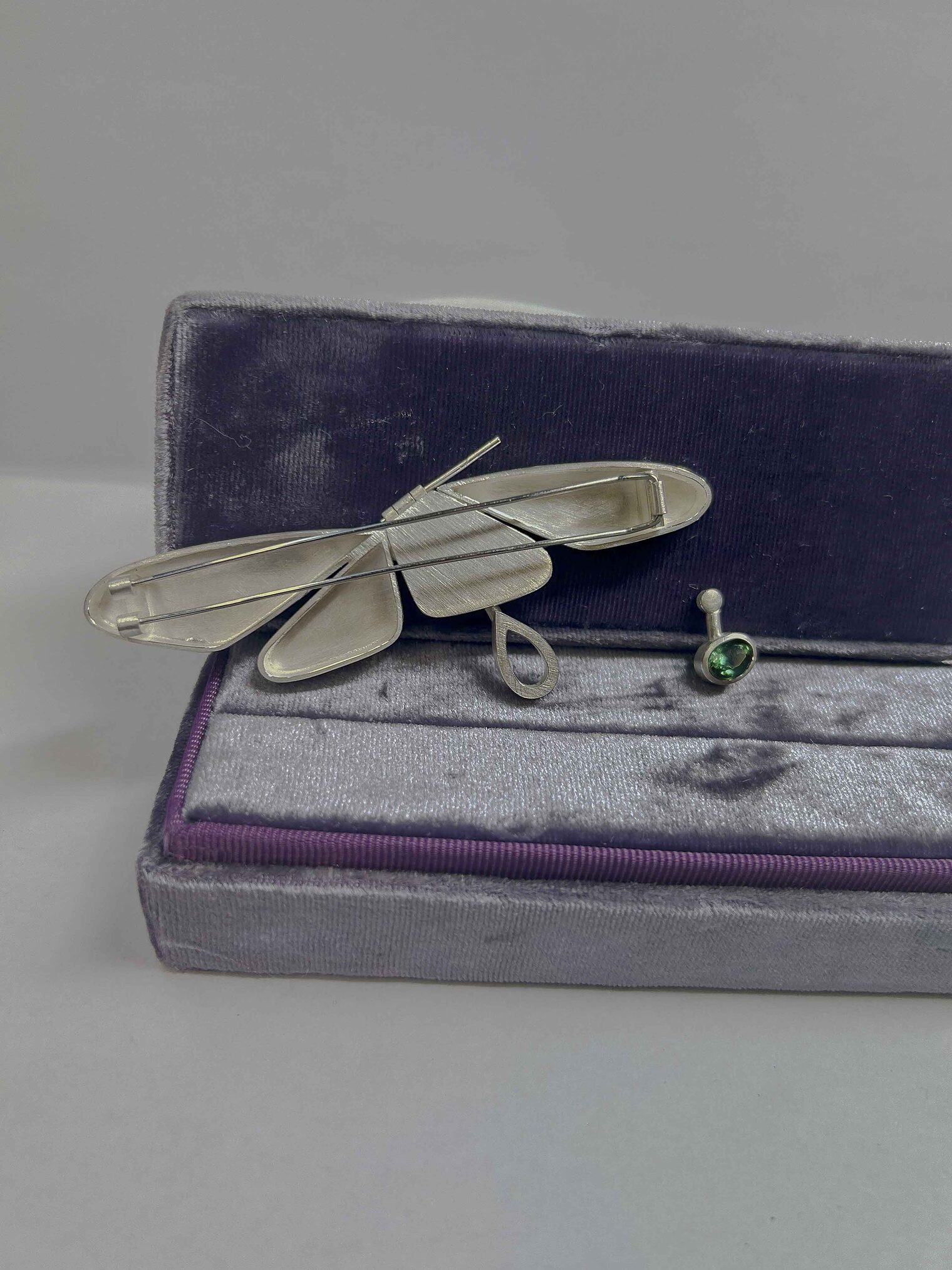 Schmuckstück in Schatulle mit Ähnlichkeit zu Schmetterling, grüner Stein eingefasst