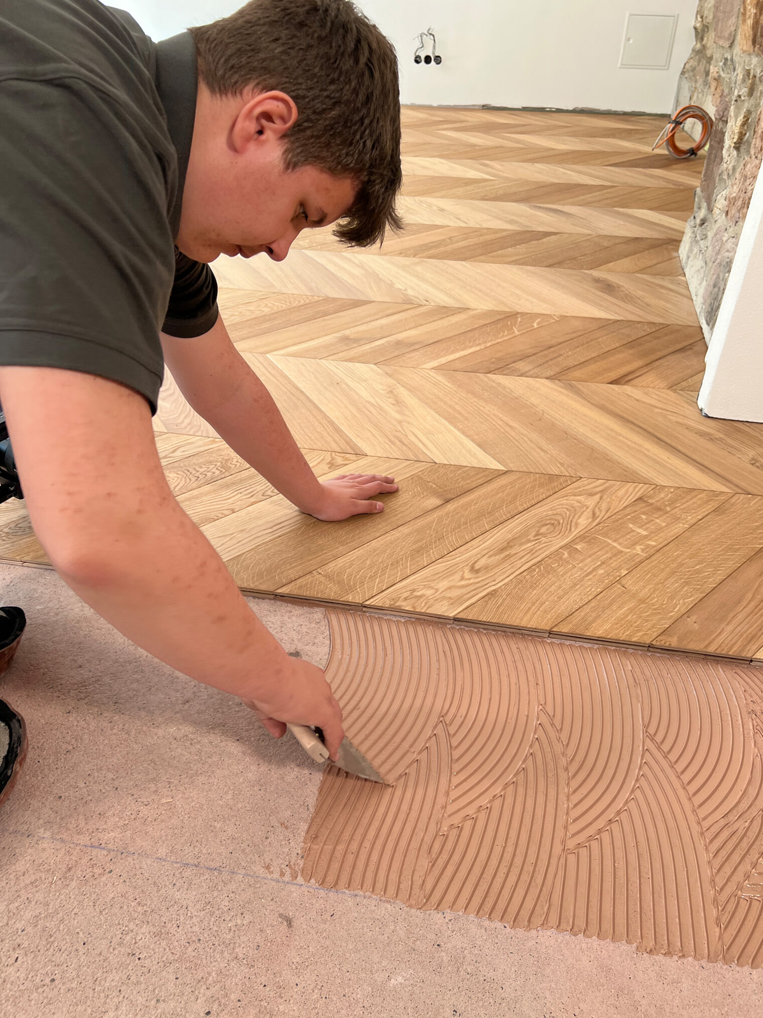 Parkettleger am Boden, trägt Leim für Holz auf