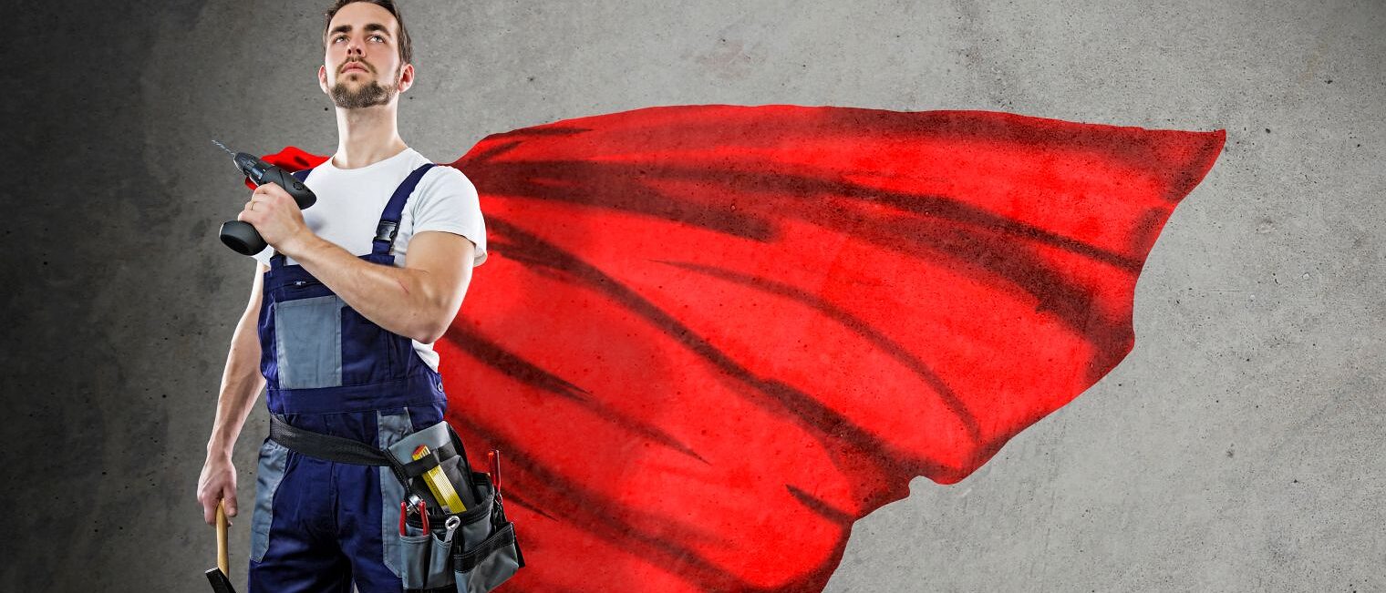 Handwerker in Blaumann mit rotem Cape und Bohrmaschine in der Hand