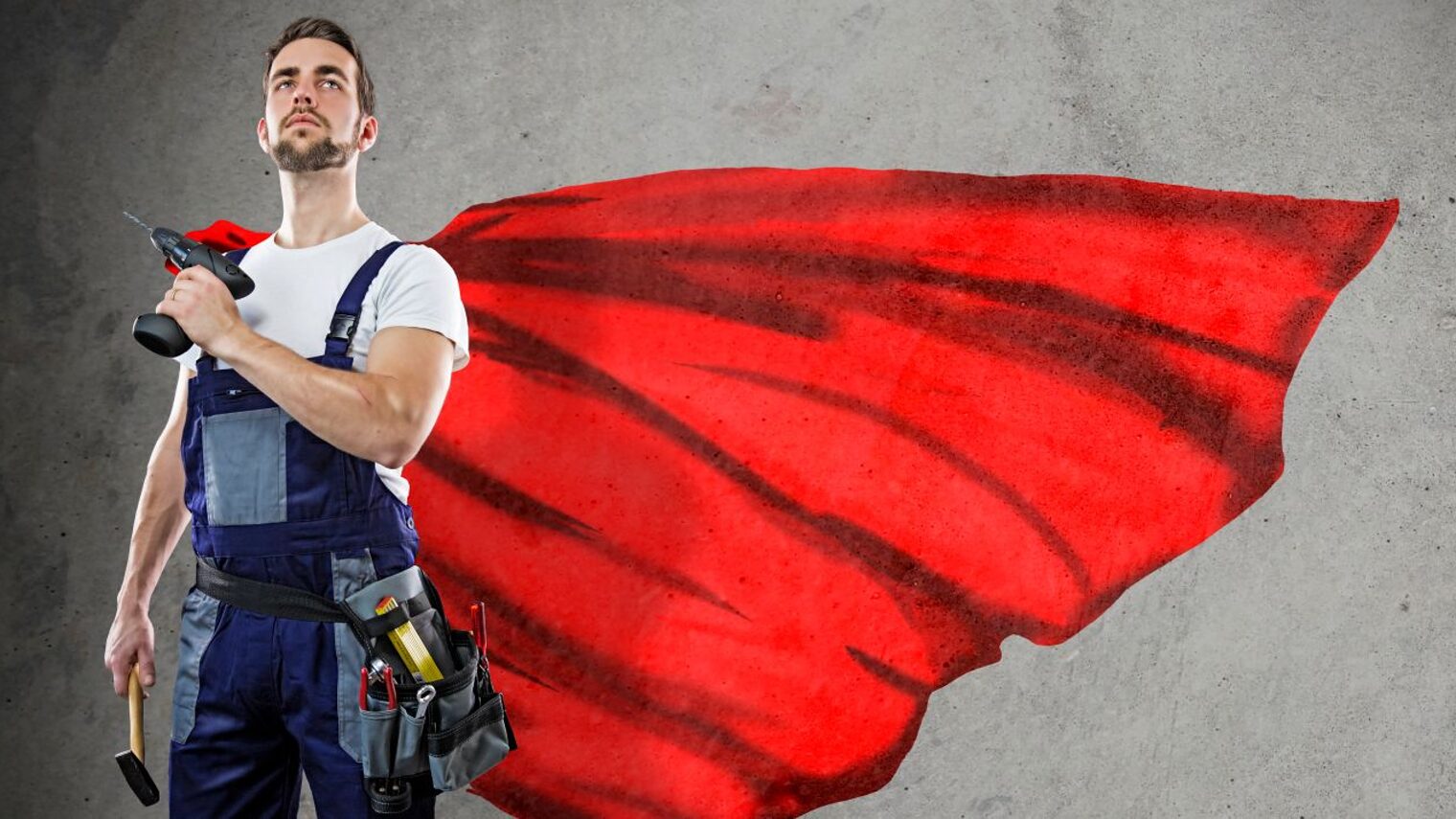 Handwerker in Blaumann mit rotem Cape und Bohrmaschine in der Hand