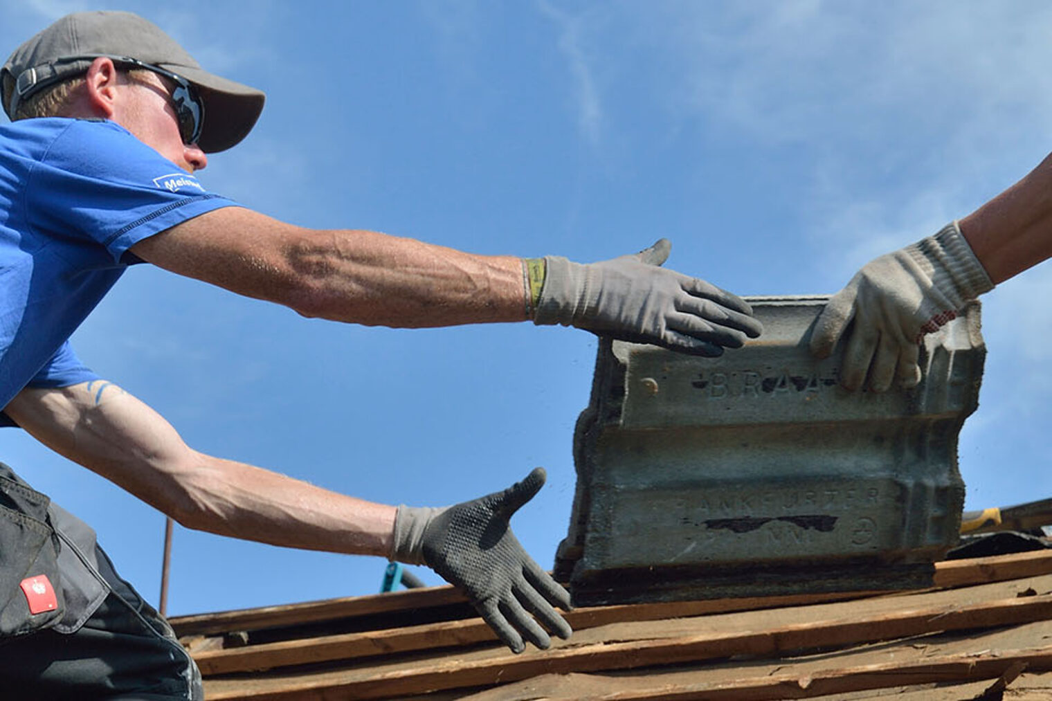 Dachdecker auf Dach reichen sich Ziegeln zu