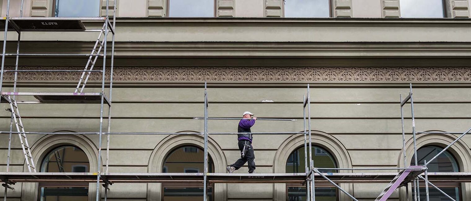 Totale von Gerüst an Gebäude mit einem darauf laufenden Gerüstbauer