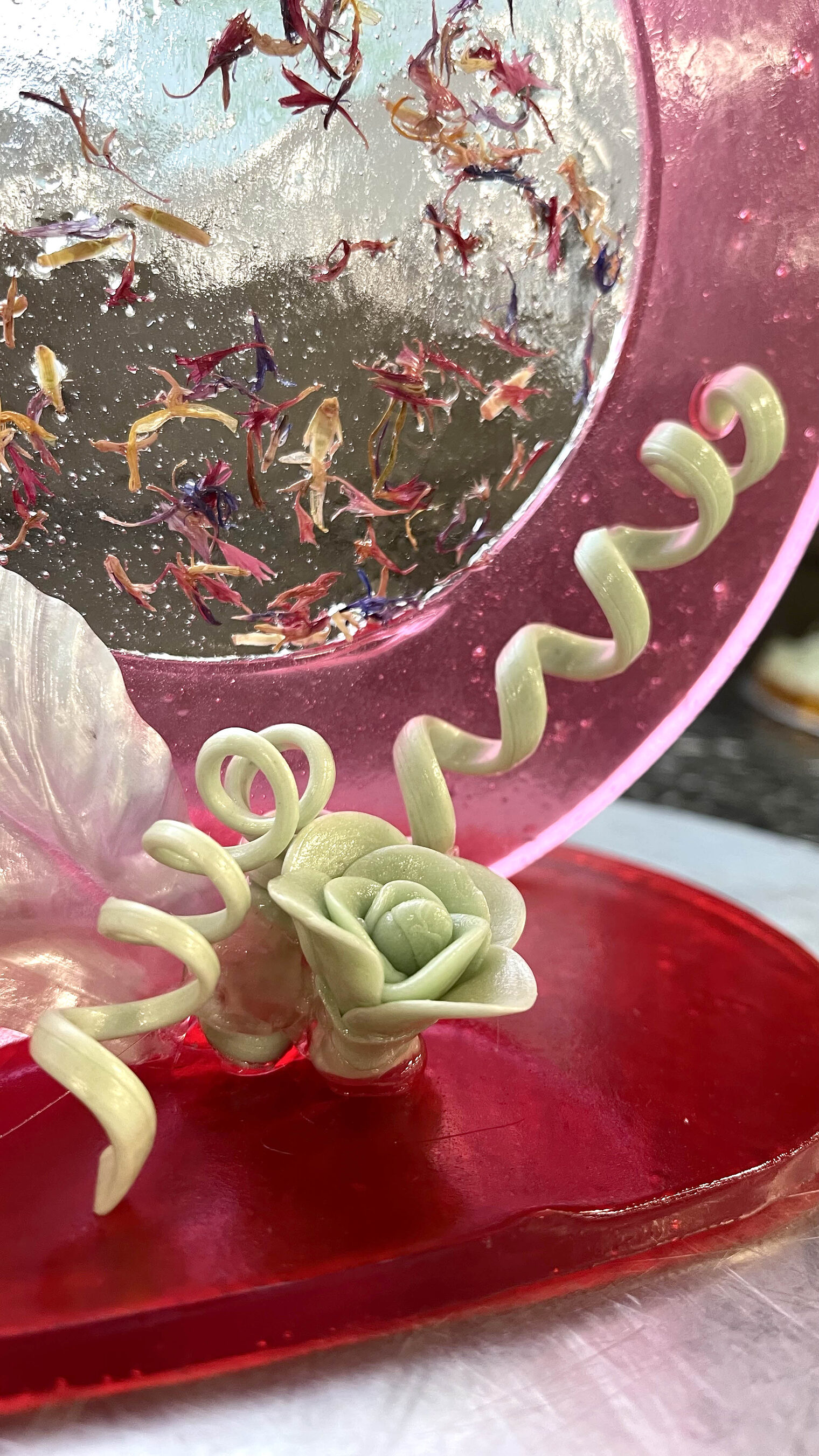 Eine kunstvolle Zuckerskulptur bestehend aus Spiralen aus rotem Zucker, einem weißen Blütenblatt und einer Zuckerrose.