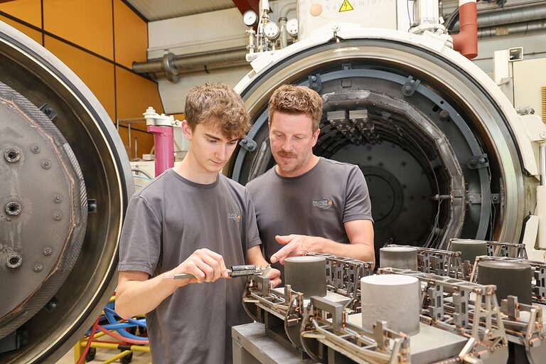 Zwei Personen vermessen ein Bauteil vor einem Vakuum-Lötofen